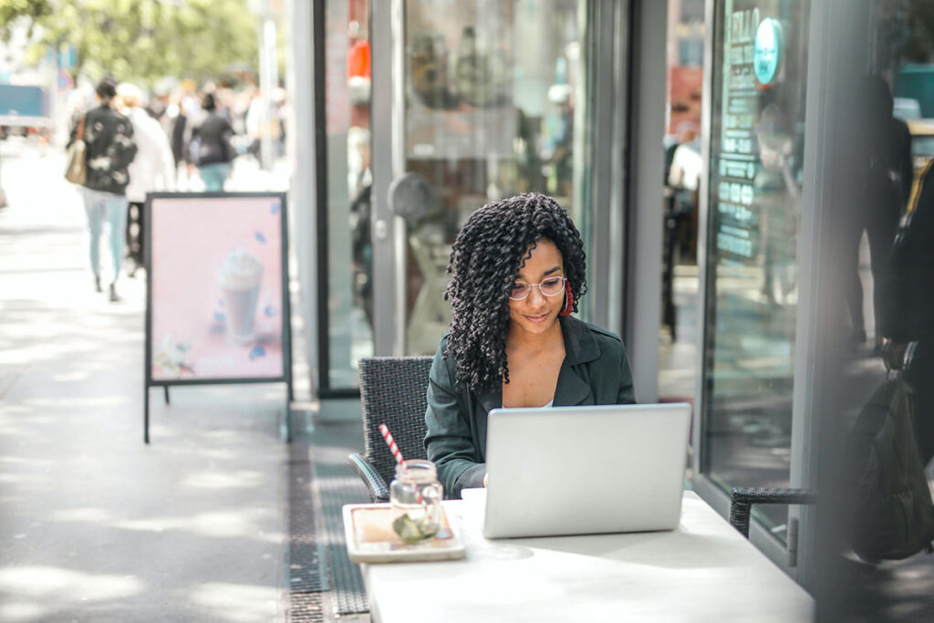 ethnic young woman using laptop to start an online business while having tasty beverage in modern street cafe